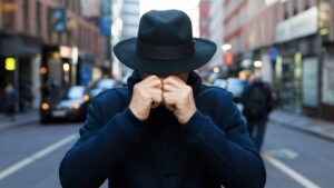 Detektyw Warszawa – mężczyzna w kapeluszu zasłania twarz na ulicy miasta